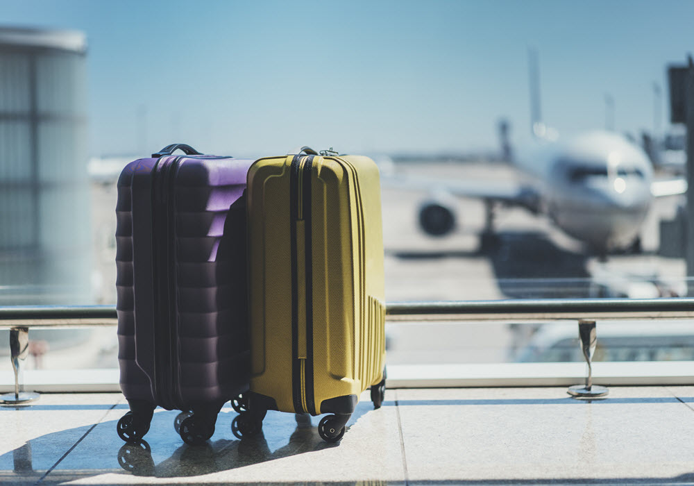 Suitcases at the airport next to glass wall overlooking a plane.