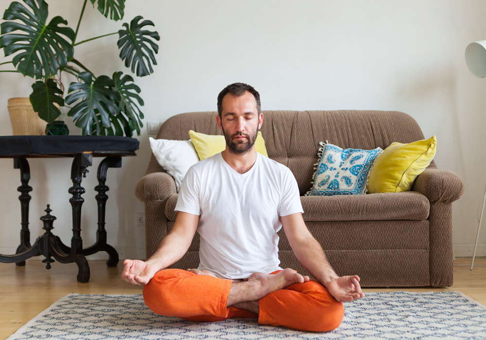 Man practicing a meditating yoga pose in his apartment home.