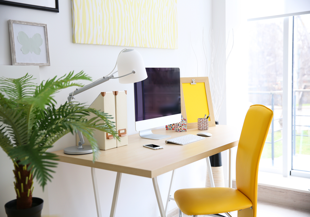 Home office in bedroom featuring medium plant to the left of desk.