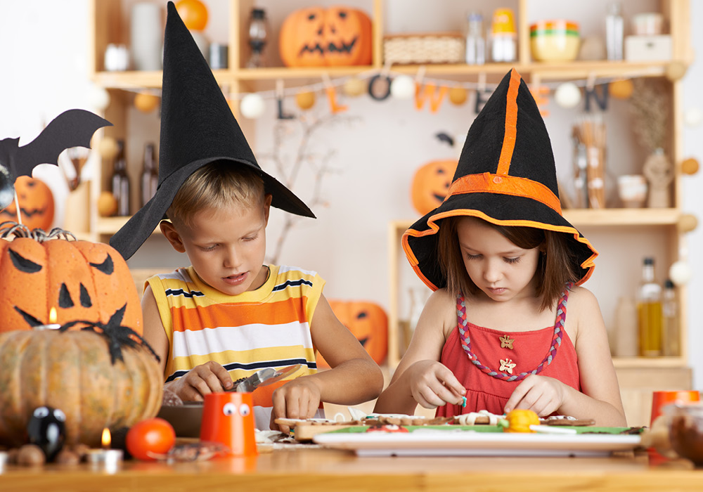 Two kids in witches' hats decorating their Halloween treats.