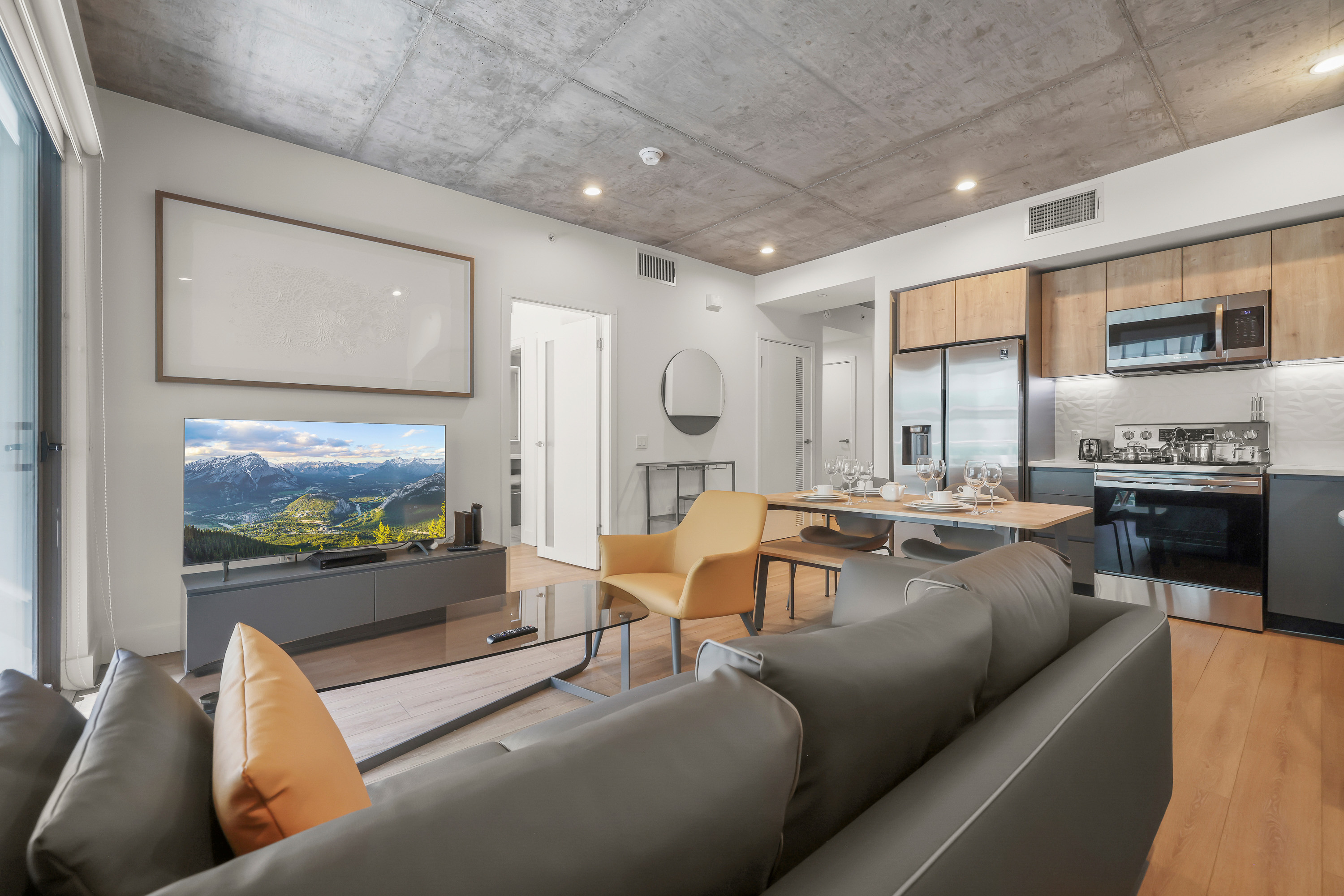 Modern Skylux on Wilshire apartment interior with an open living and dining area, stainless-steel kitchen appliances, large windows, and exposed concrete ceilings.