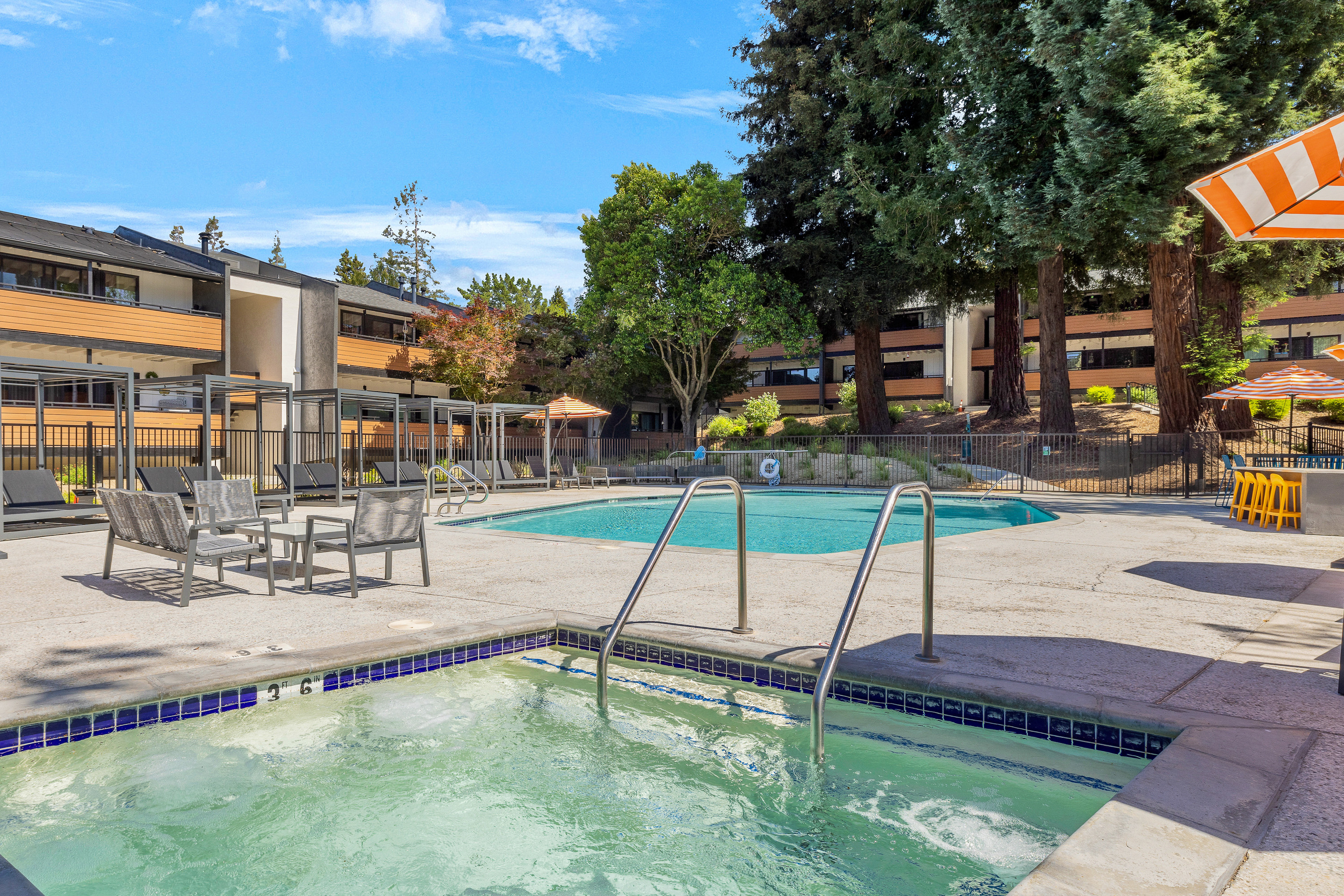 Renovated pool and spa at Lafayette Highlands with lounge seating, cabanas, striped umbrellas, and landscaped surroundings.